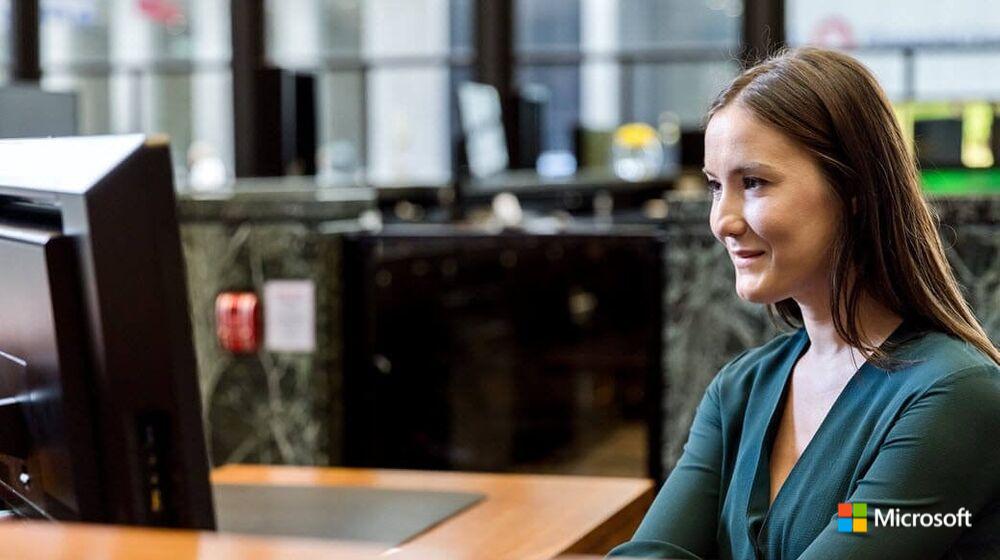 Brown haired woman at desk smiles looking towards computer screen. 