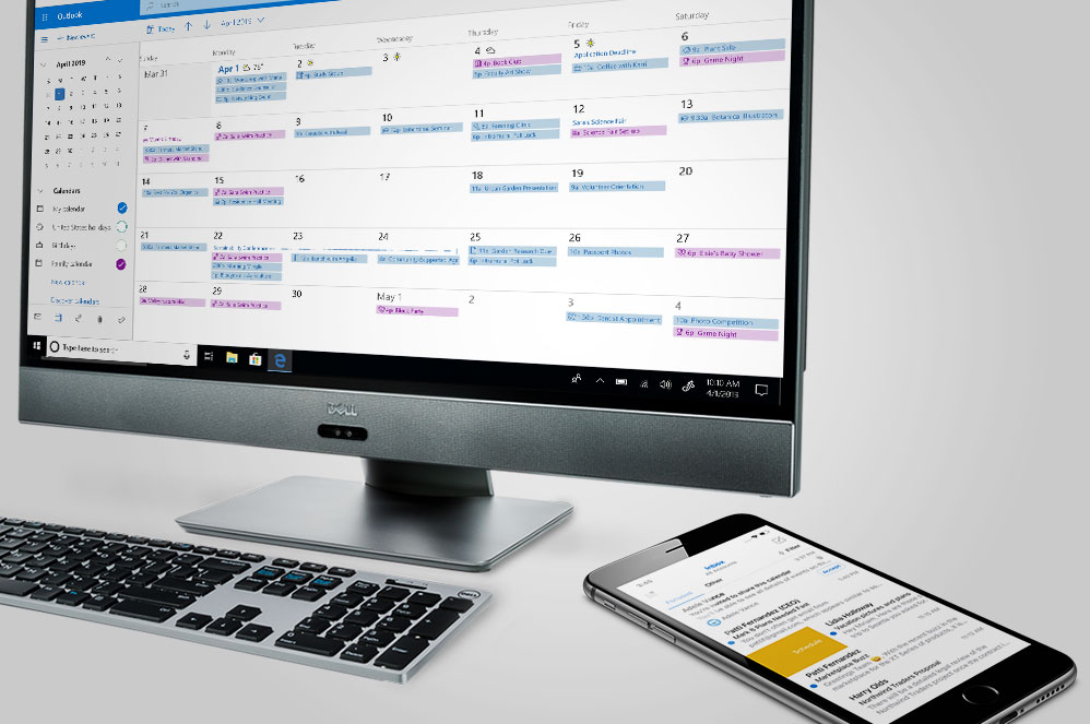 A Windows 10 all in one showing an Outlook screen while sitting next to a phone showing the Outlook app