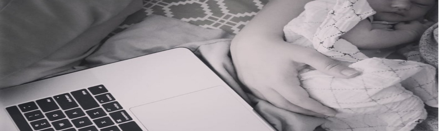 Newborn baby in mothers arms next to laptop computer